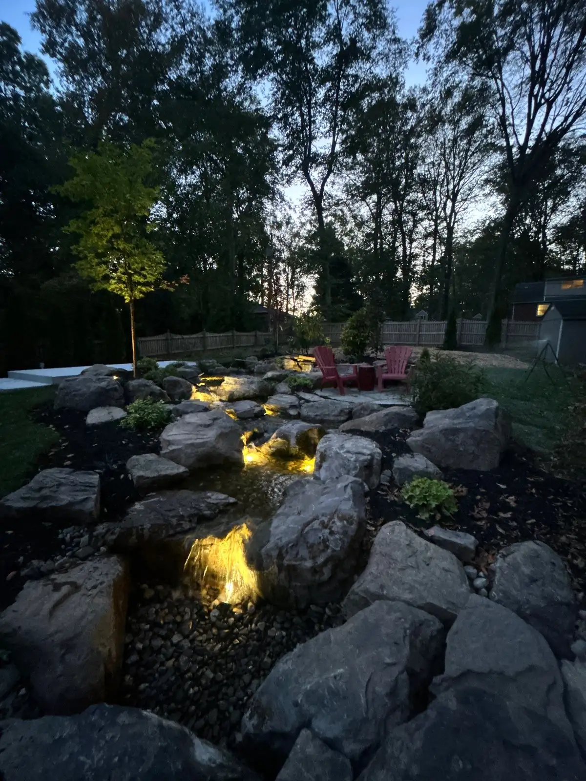 LED-lit waterfall and pond at night with natural boulders in Hockessin, Delaware